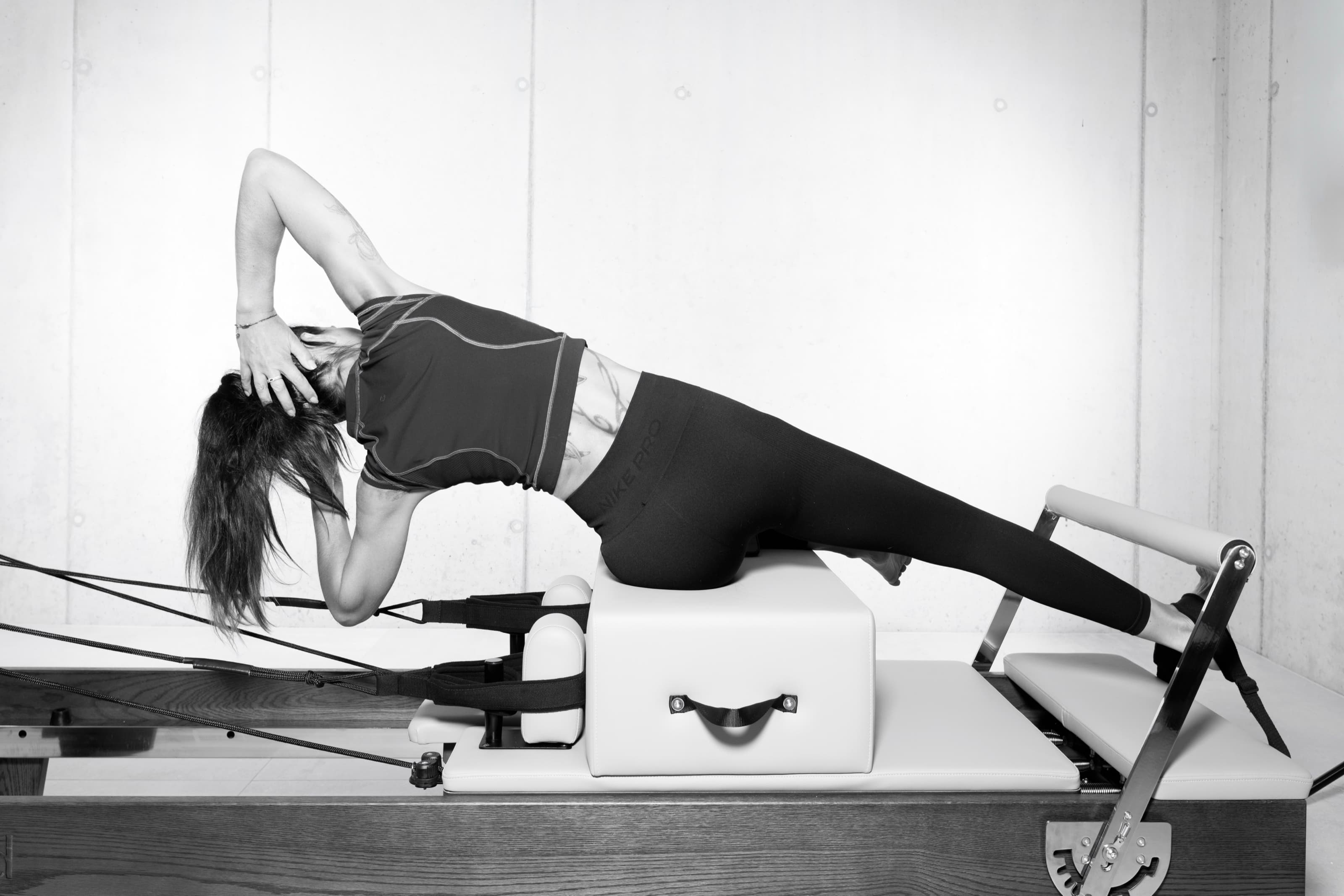 Lili en planche latérale sur la box du Reformer, un bras derrière la tête