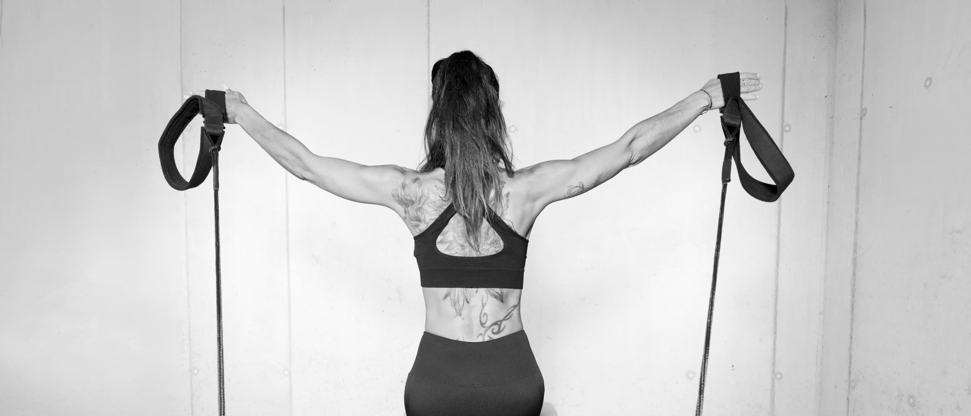 Lili de dos sur le Reformer, bras ouverts dans les sangles